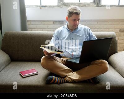 Distance education. A young guy on a sofa at home studying with a laptop. Stock Photo