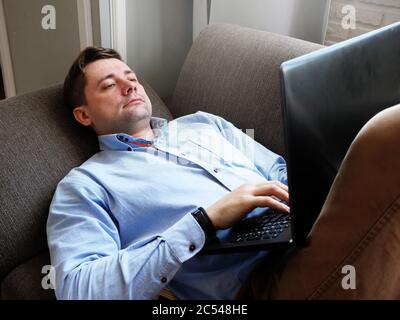 Remote work. A man at home on the couch works with a laptop. Stock Photo