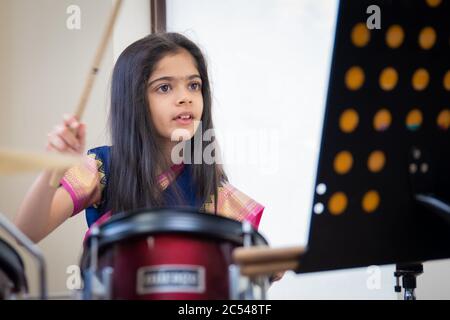 School age British Indian girl playing the drums in a saree. Stock Photo
