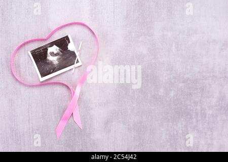 Ultrasound image of a baby with a pink ribbon in the form of a heart on a gray background with place for text Stock Photo