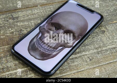 Viersen, Germany - June 30. 2020: Close up of isolated mobile phone screen with human skull paint on wood table Stock Photo