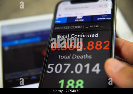 Viersen, Germany - June 30. 2020: Close up of mobile phone screen hold by male hand with counter of John Hopkins university showing numbers of worldwi Stock Photo