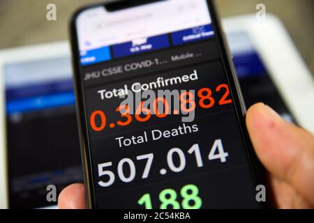 Viersen, Germany - June 30. 2020: Close up of mobile phone screen hold by male hand with counter of John Hopkins university showing numbers of worldwi Stock Photo