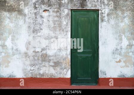 Old green door in a grunge wall. Vintage, retro door. Red floor. Stock Photo