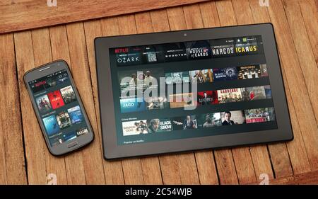 Netflix´s website open on tablet and cell phone screen. In these can see thumbnails of movies and serials. Stock Photo