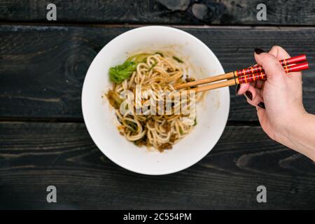 Dandan Noodles on chopsticks. Dan Dan Noodles is a spicy Szechuan cuisine dish commonly found in chinese street food. Ingredients include thick rice n Stock Photo
