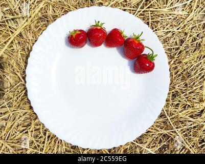 strawberries on white plate and straw background Stock Photo