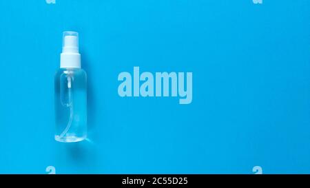Hand sanitizer transparent bottle with spray cap at the left of a blue background. Simple flat lay with copy space. Pastel paper texture. Medical concept Stock Photo