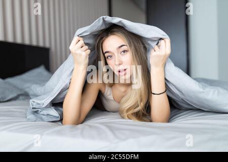 Smiling woman under a duvet in her bedroom. Closeup portrait of a beautiful young woman under the blanket. Stock Photo