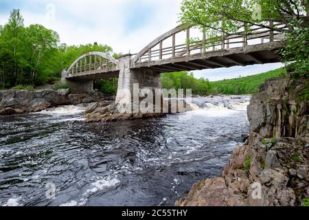 An old concrete archway bridge spans over a large salmon river with lots of rocks in the river. Stock Photo