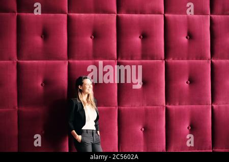 Young Business Woman Standing Against Burgundy Wall Panels Stock Photo