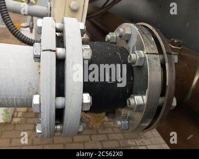 Old grey painted rubber expansion joint with cracks in the pipeline in industrial production line. Selective focus. Stock Photo