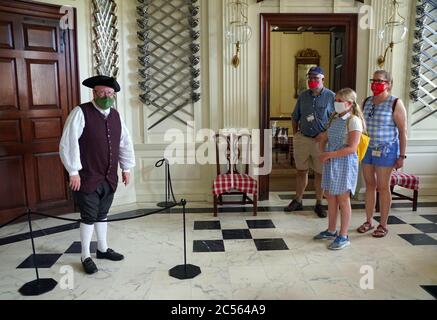Williamsburg, Virginia, U.S.A - June 30, 2020 - A man in colonial costume inside Governor's Palace assisting visitors during a tour, and everyone is w Stock Photo
