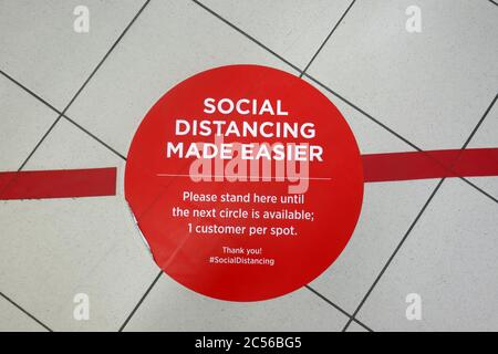 Social distancing made easier sign on floor.  A red spot on the floor advising shoppers to stand on red circle when waiting in line at a store.