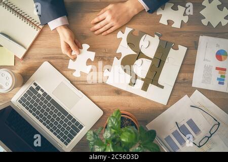 Man sitting at his workplace in the office. Top view close-up. Businessman is trying to connect couple puzzle piece. Symbol of bitcoins. Concept of bu Stock Photo