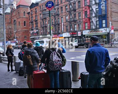 New York, NY - March 27, 2017:  Travellers arriving at the Port Authority bus terminal wait on the sidewalk outside for cabs and city buses. Stock Photo