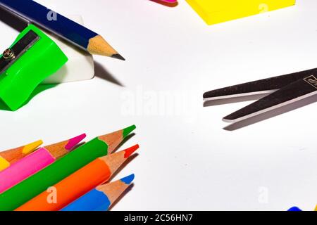 Closeup shot of colored pencils, scissor, eraser, and a notepad on a white background Stock Photo