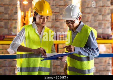 Asian warehouse manager discuss with warehouse worker using archboard to assign job with distribution warehouse in background. Reopening business ware Stock Photo