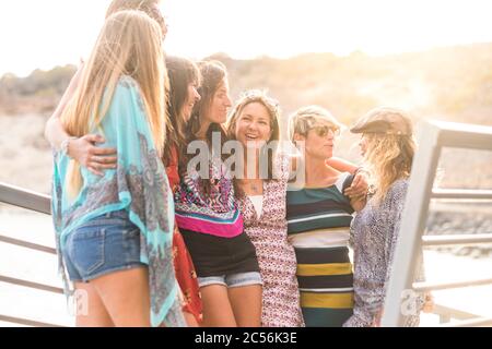 group of seven nice and beautiful caucasian girls young women have fun and laugh and smiles outdoor near the ocean during the sunset. backlight paople Stock Photo