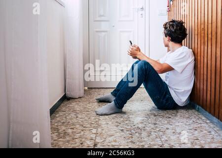 People inside home for stayhome lockdown emergency coronavirus - young man sit down on the. floor with a phone looking at the door hope and wait to go Stock Photo