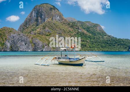 Palawan island, Philippines. Low angle view of traditional filippino boat in shallow water in El Nido bay. Epic Cadlao island in background. Stock Photo