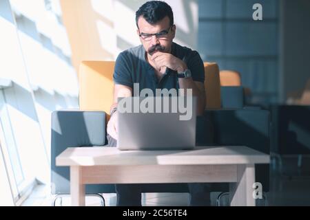 Concentrated toughtful man is looking to laptop screen  in a modern office Stock Photo