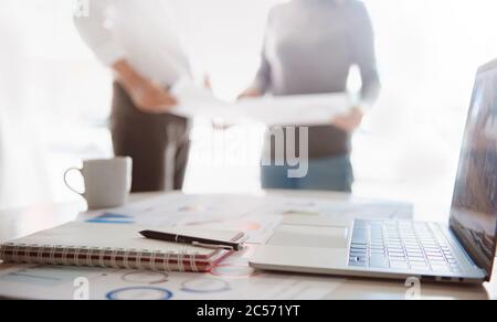 blur Close-shot of a pen and computer displaying financial data, business group standing in the background Stock Photo