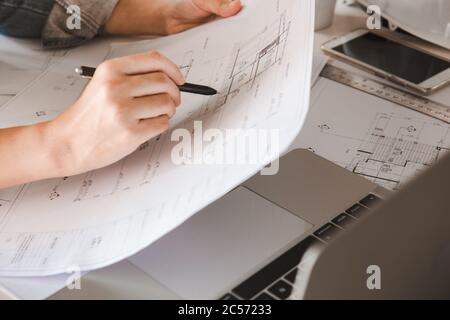 Engineers holding a pen pointing to a building on a blueprint and using a computer laptop to  to planning project schedule. Engineering and constructi Stock Photo
