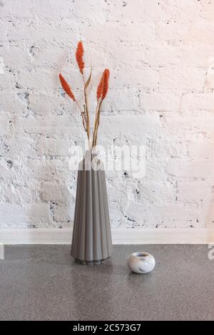 Simple modern vase with orange flowers against white brick wall Stock Photo