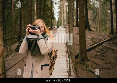 Portrait woman using retro camera on footbridge in woods Stock Photo