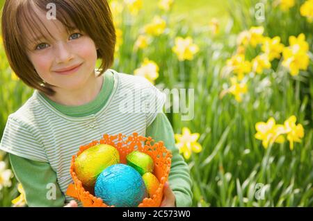 Portrait smiling girl with Easter egg candy in daffodil field Stock Photo