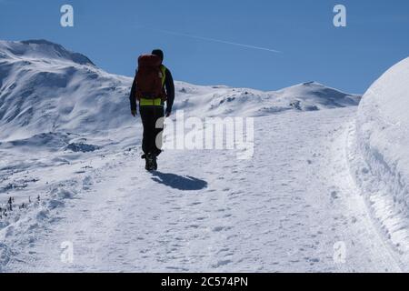 Man with backpack hiking up sunny, snowy mountain path, Muestair, Switzerland Stock Photo