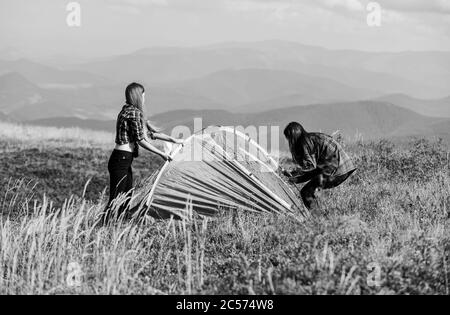 Girls set up tent on top mountain. Camping skills concept. Camping and hiking. In middle of nowhere. Temporary housing. Vacation in mountains. Camping trip. Helpful to have partner for raising tent. Stock Photo