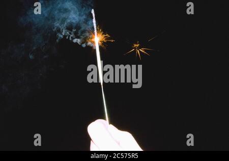 Hand holding sparkler against black background Stock Photo