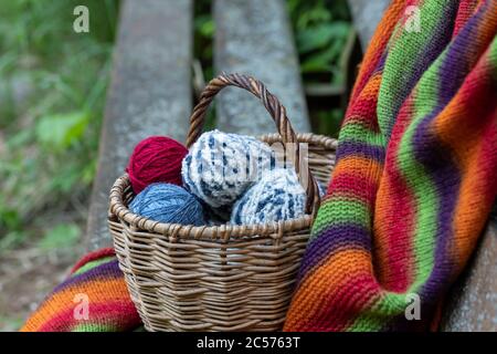 Red, blue and white woolen balls in a wicker basket on a multi-colored knitted blanket. Natural background. Horizontal poster with copy space. Yarn fo Stock Photo