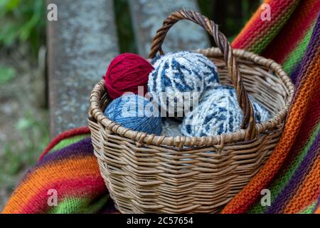Red, blue and white woolen balls in a wicker basket on a multi-colored knitted blanket. Natural background. Horizontal poster with copy space. Yarn fo Stock Photo