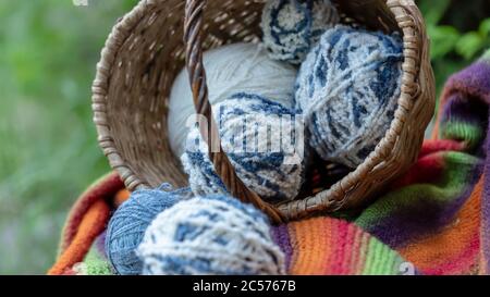 blue and white wool balls in a wicker basket on a multi-colored knitted blanket. Natural background. Horizontal poster with copy space. Yarn for knitt Stock Photo