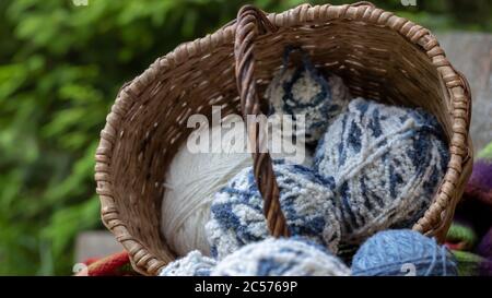 blue and white wool balls in a wicker basket on a multi-colored knitted blanket. Natural background. Horizontal poster with copy space. Yarn for knitt Stock Photo