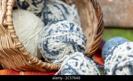 blue and white wool balls in a wicker basket on a multi-colored knitted blanket. Natural background. Horizontal poster with copy space. Yarn for knitt Stock Photo