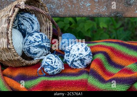blue and white wool balls in a wicker basket on a multi-colored knitted blanket. Natural background. Horizontal poster with copy space. Yarn for knitt Stock Photo