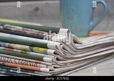Closeup of the stack of newspapers with a cup of coffee isolated on a wooden surface Stock Photo
