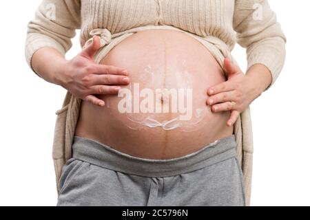Close-up of young pregnant woman applying moisturizer on her belly as care routine concept isolated on white background Stock Photo