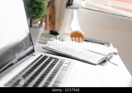 Selective focus shot of an open notebook planner next to a laptop on a white table Stock Photo