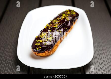 Chocolate eclaire with pistachio nuts on a white plate Stock Photo