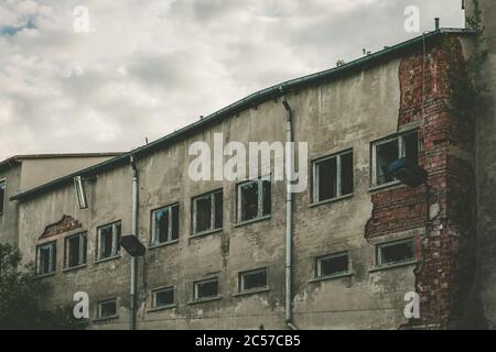 Old worn down building with grey walls and bricks sticking out on one side with metal drains Stock Photo