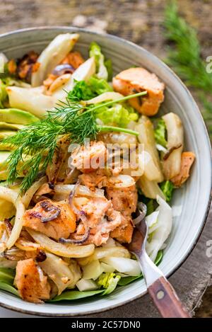 Main meal, salad bowl with salmon, oven-roasted fennel, fried onion, avocado, coconut yoghurt dressing Stock Photo