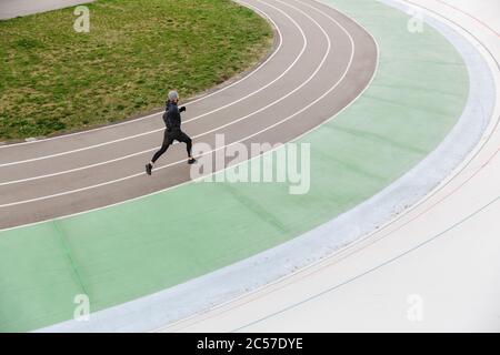 Confident young fit sportsman running on the race track at the stadium outdoors Stock Photo