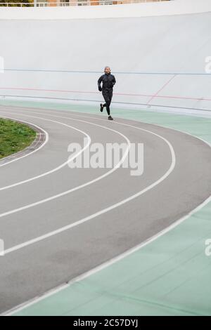 Confident young fit sportsman running on the race track at the stadium outdoors Stock Photo