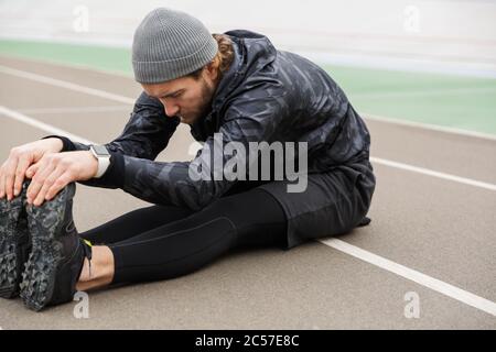 Motivated young fit sportsman working at the stadium racetrack, doing stretching exercises Stock Photo