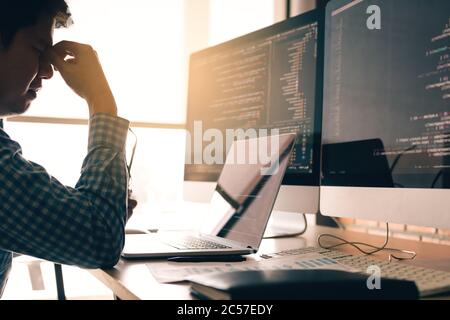 Man programmers are stressed and hand holding nose with headache at the office while working analyzing on desk in code at office room. Stock Photo